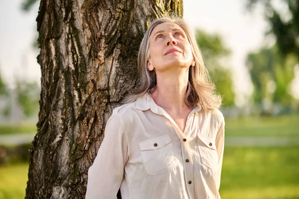 Mujer apoyada contra el árbol mirando hacia arriba — Foto de Stock