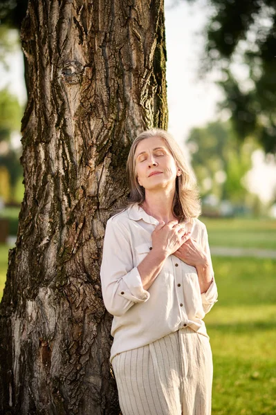 Vrouw gevouwen handpalmen op de borst in de buurt van boom — Stockfoto