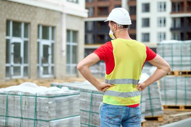 Ahşap paletlere istiflenmiş tuğlalara bakan inşaatçı.