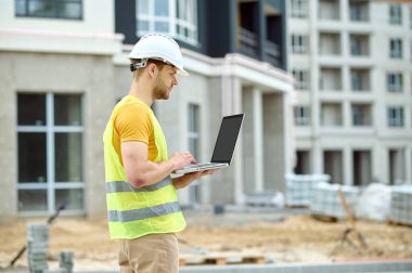 Dizüstü bilgisayarı üzerinde çalışan koruyucu başlıklı ciddi bir adam.