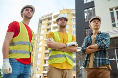 Uzağa bakan kasklı üç ciddi yakışıklı işçi.