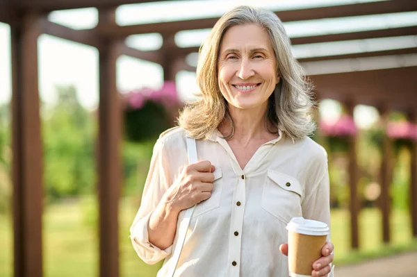 Mujer adulta con café disfrutando pasear por el parque —  Fotos de Stock