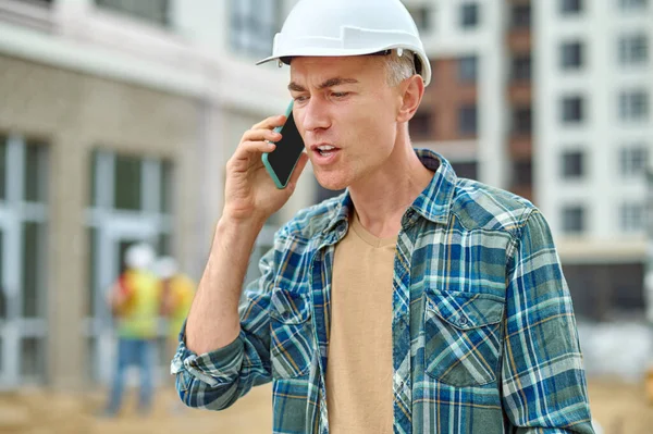 灰白头发的男性建筑者在室外用手机交谈 — 图库照片