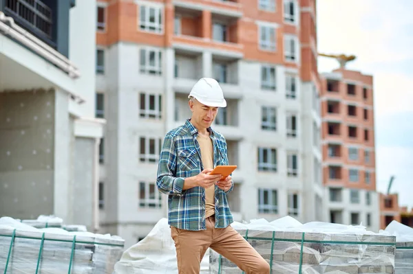 Ingeniero de construcción enfocado mirando el gadget en sus manos —  Fotos de Stock