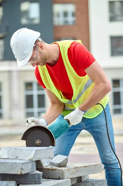 Trabajador concentrado en un casco y gafas inclinadas sobre materiales de construcción —  Fotos de Stock