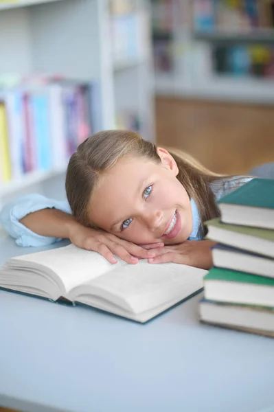 Vidám, csinos iskoláslány fekszik egy könyvtári könyvön. — Stock Fotó