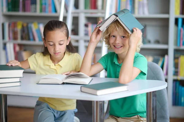 En flitig flicka och en lättsam pojke sitter på biblioteket — Stockfoto