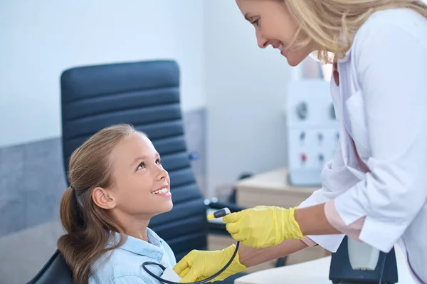 Audiólogo sonriente con un dispositivo médico inclinado hacia un paciente — Foto de Stock