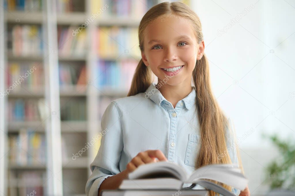 Happy cute schoolchild standing at a desk with books