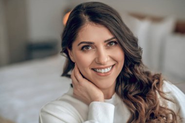 Beyaz bluzlu, güzel, uzun saçlı bir kadın gülümsüyor.