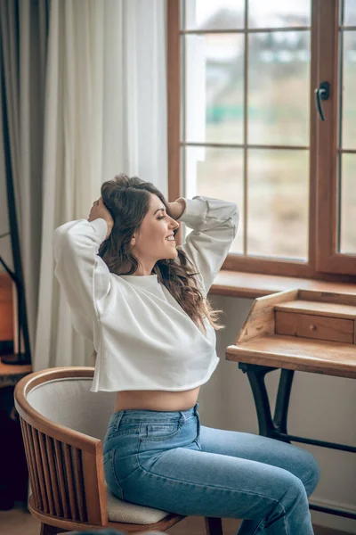 Bella giovane donna dai capelli lunghi in una camicetta bianca seduta alla finestra — Foto Stock