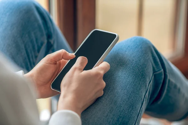 Primer plano de una mujer en jeans con un smartphone en las manos — Foto de Stock