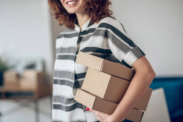 Sonriente trabajadora alegre con paquetes de pie en el interior — Foto de Stock