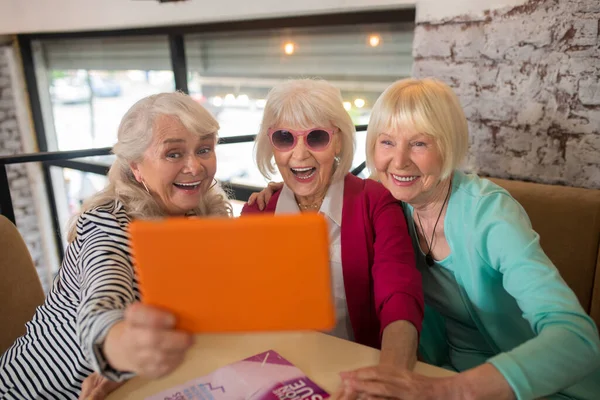 Senhoras idosas bem parecidas fazendo uma chamada de vídeo e parecendo animadas — Fotografia de Stock