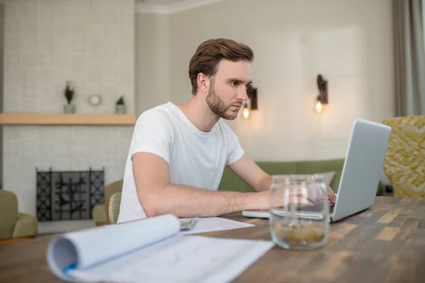 Jovem barbudo trabalhando em um laptop e olhando concentrado — Fotografia de Stock