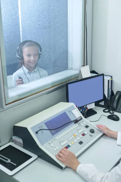 Chica en auriculares detrás de vidrio y manos de otorrinolaringólogo — Foto de Stock