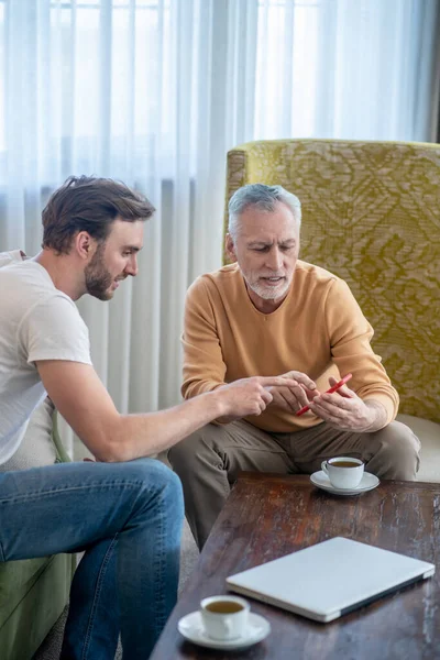 Jeune homme enseignant à son père comment utiliser un nouveau smartphone — Photo