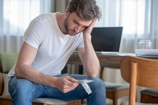 Un hombre sentado con el dinero en las manos y mirando molesto — Foto de Stock