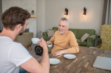 Masada oturan iki adam, çay içip sohbet ediyorlar.