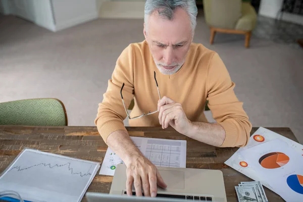 Grijsharige man werkt aan een laptop en ziet er druk uit — Stockfoto