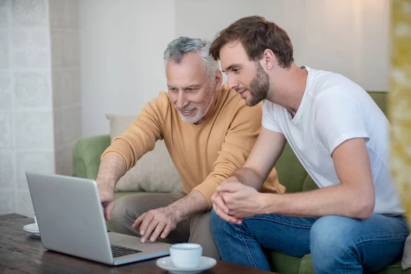 Young man and his dad watching something online and looking involved — Stock Photo, Image