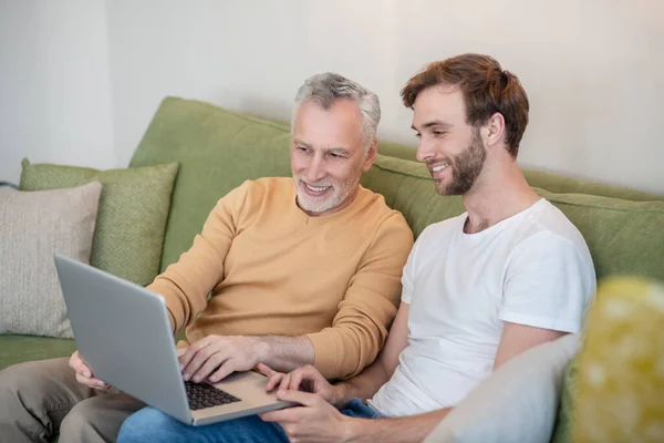 Young man and his dad watching something online and looking involved — Stock Photo, Image