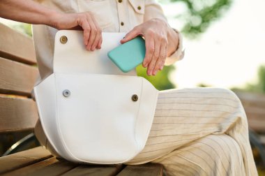 Kadın elleri akıllı telefonu açık çantaya koyuyor.