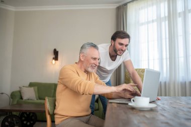 Laptopun başındaki odada laptoptan bir şey izleyen iki adam.