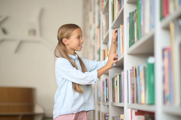 Fiatal lány keresi a megfelelő könyveket — Stock Fotó