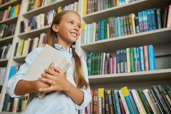 Vidám lány tankönyvekkel a kezében a könyvtárban. — Stock Fotó