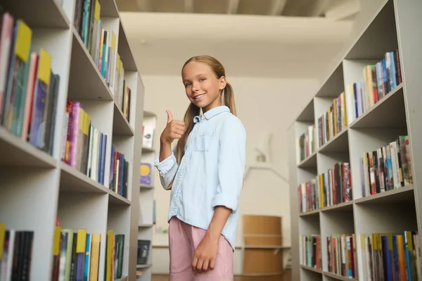 Радостная молодая школьница позирует перед камерой в библиотеке — стоковое фото