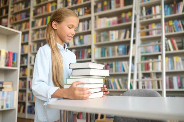 Kényelmes iskolásgyerek tankönyveket tesz az asztalra. — Stock Fotó