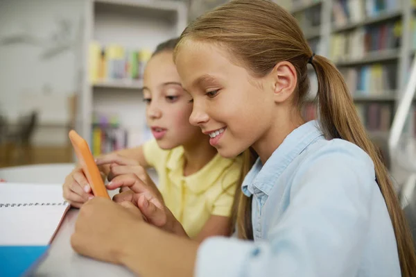 Dos compañeros de clase usando un gadget en una biblioteca pública — Foto de Stock