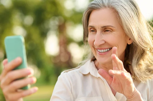 Femme joyeuse regardant affablement dans le smartphone — Photo