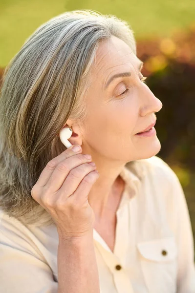 Mujer sosteniendo auriculares cerca de la oreja al aire libre — Foto de Stock