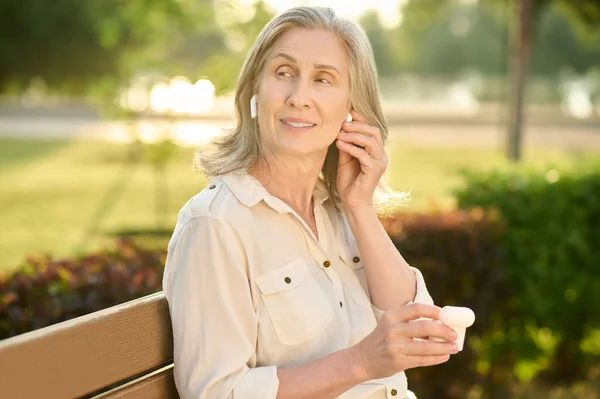 Mujer adulta linda con auriculares en el banco — Foto de Stock