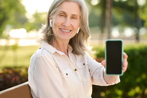 Good looking retirement age woman showing smartphone