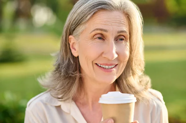 Оптимистичная улыбающаяся женщина с кофе на открытом воздухе — стоковое фото