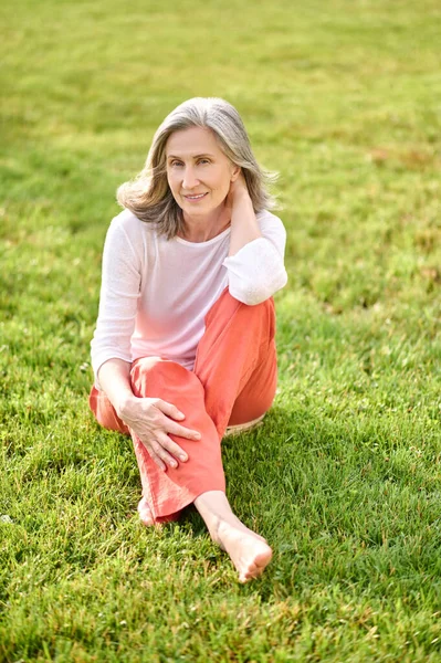 Çıplak ayaklı bir kadın çimenlerde oturuyor. — Stok fotoğraf