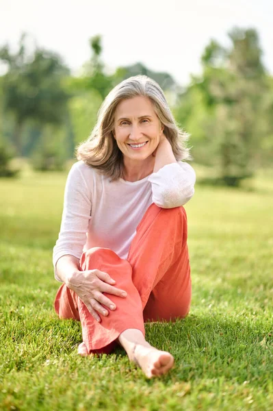 Glimlachende vrouw op blote voeten zittend op gras — Stockfoto