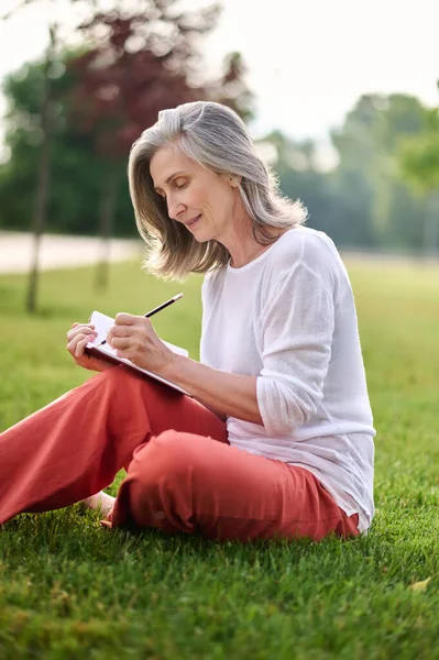 Mulher escrevendo em caderno na grama no parque — Fotografia de Stock