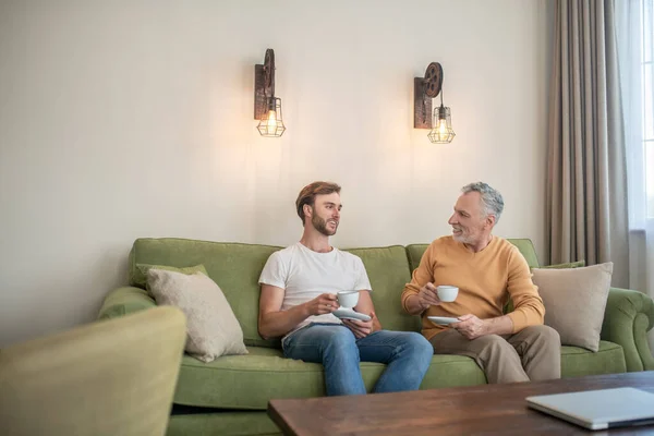 Двое мужчин сидят на диване и пьют чай — стоковое фото