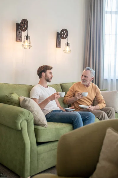 Two men sitting on the sofa and having tea — Stock Photo, Image