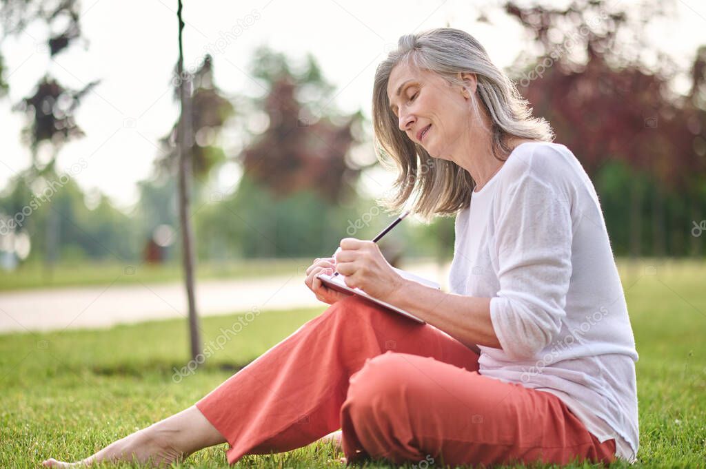Focused adult woman writing in notebook on nature