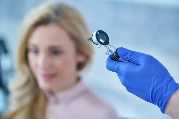 Otoscope in hand of doctor and woman in distance — Stock Photo, Image