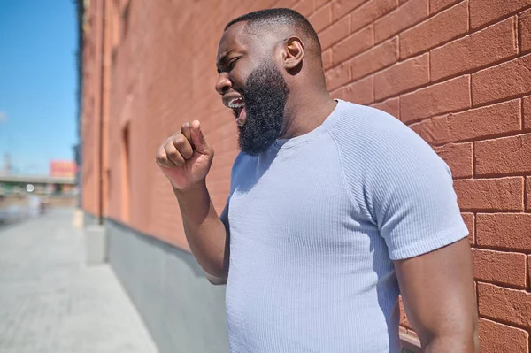 Un hombre de piel oscura con una camiseta blanca y jeans cerca de la pared de ladrillo — Foto de Stock