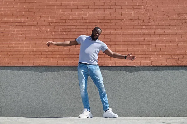 Un hombre de piel oscura con una camiseta blanca y jeans cerca de la pared de ladrillo —  Fotos de Stock