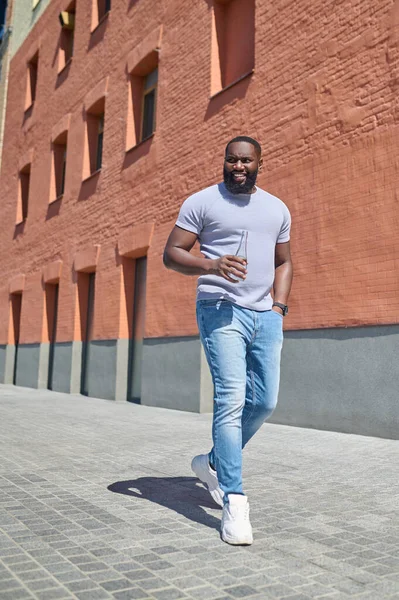 Un hombre de piel oscura con una camiseta blanca caminando por la calle — Foto de Stock