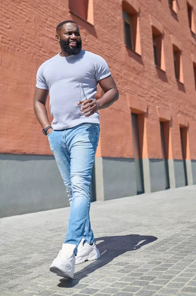 Un hombre de piel oscura con una camiseta blanca caminando por la calle —  Fotos de Stock