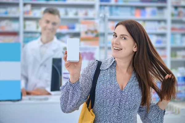 Счастливая женщина трогает волосы стоя в аптеке — стоковое фото
